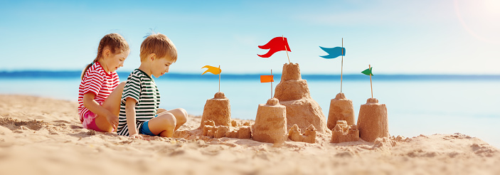 Group of Diversity little child boy and girl friends playing beach toy and build a sand castle together at tropical beach. Children kids enjoy and fun outdoor lifestyle travel ocean on summer holiday vacation.
