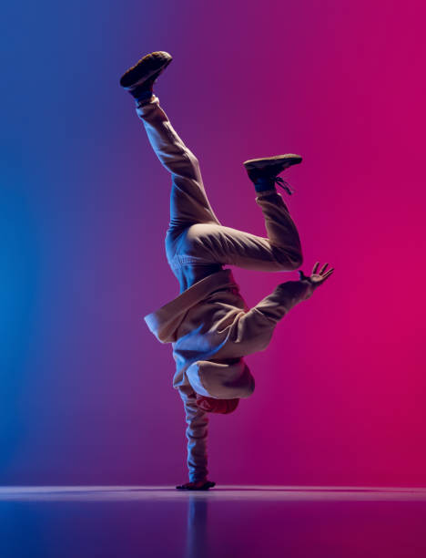 studioaufnahme eines jungen flexiblen sportlichen mannes, der breakdance in wei�ßem outfit auf rosa blauem hintergrund tanzt. konzept von aktion, kunst, schönheit, sport, jugend - breakdancing stock-fotos und bilder