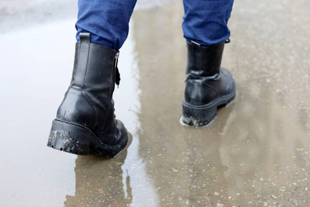 istock Female legs in black leather boots with reflection in puddle on a street 1371309626