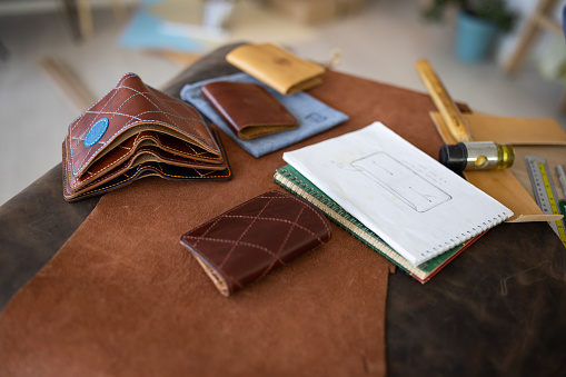Handmade leather wallets and sketch for new wallet on table in leather crafting workshop