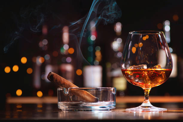 Glass of whiskey or cognac with ice cubes and smoking cigar Glass of whiskey or cognac with ice cubes and smoking cigar and on bar counter cigar photos stock pictures, royalty-free photos & images