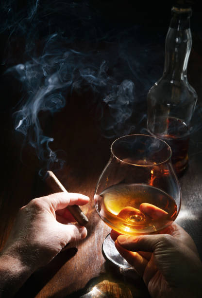 mani maschili con bicchiere di whisky o brandy e sigaro fumante - cigar whisky bar cognac foto e immagini stock