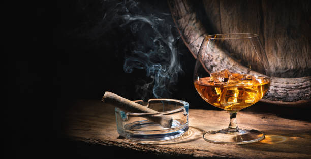 bicchiere di whisky con sigaro fumante e cubetti di ghiaccio davanti alla vecchia botte - cigar whisky bar cognac foto e immagini stock