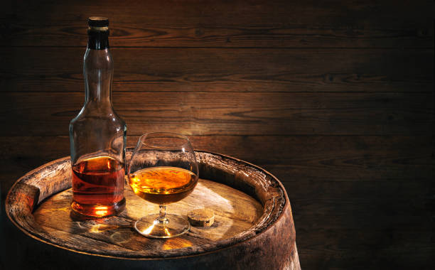 bicchiere di whisky o cognac con bottiglia su botte di legno vintage - brandy foto e immagini stock