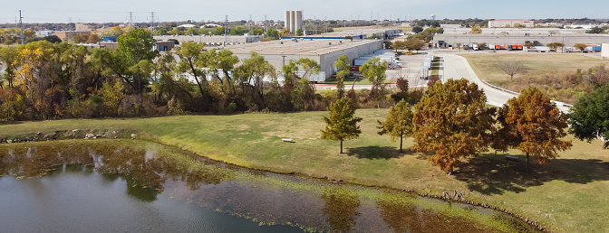 Panorama aerial view lakeside large commercial warehouse in industrial district Carrollton Texas, USA. Mixed use zoning with facility service building, purchasing, transportation near lily pad pond