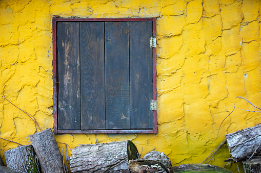 Old board and glassless window on yellow stone wall.