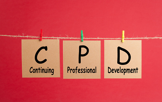 Acronym of CPD- Continuing Professional Development written over note with clip hanging on red background. Business and education concept.