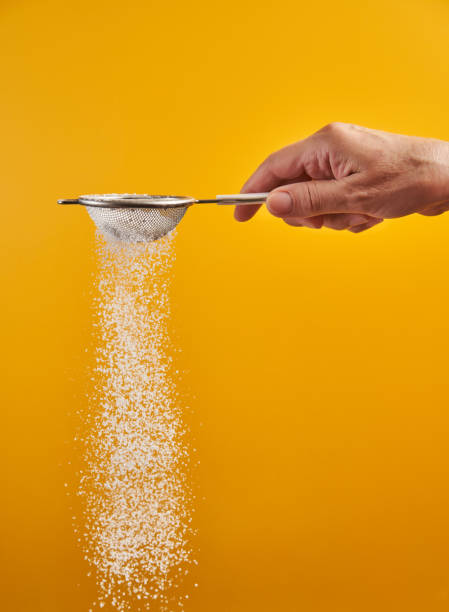Sprinkling icing sugar on yellow Woman's hand sprinkling powdered sugar with a sifter, isolated on yellow background sprinkling powdered sugar stock pictures, royalty-free photos & images