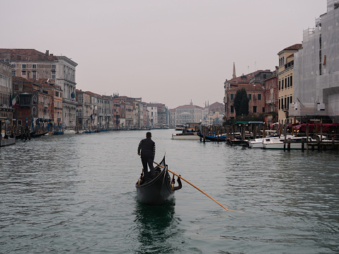 Venice, Italy - January 4 2022: Gondolier Boatman Rowing Gondola on Canal Grande near Rialto Bridge in Winter