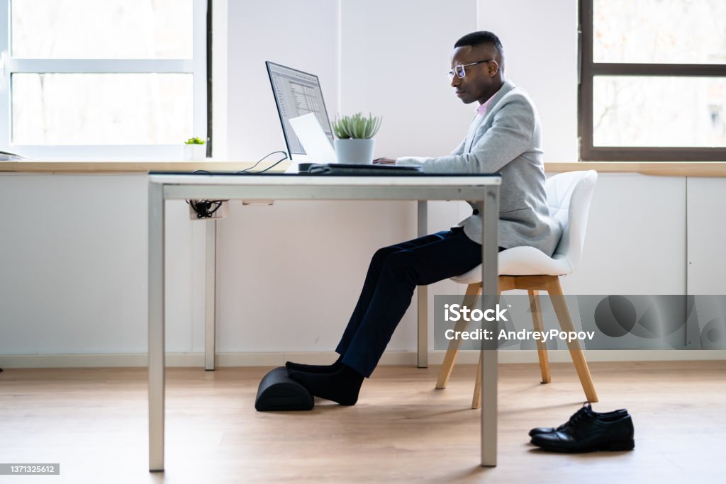 Worker Using Footrest To Reduce Back Strain Worker Using Footrest To Reduce Back Strain And Feet Fatigue Ottoman Stool Stock Photo