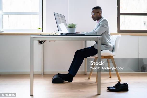 Worker Using Footrest To Reduce Back Strain Stock Photo - Download Image Now - Ottoman Stool, Desk, Computer