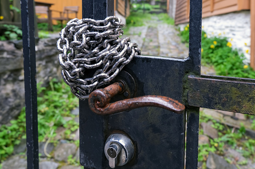 Higher angle view close-up of a rustic metal door locked with a padlock and iron chain with a blurred background
