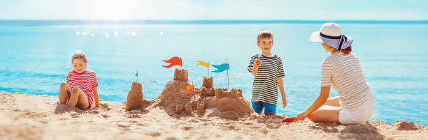 mother with son and daughter sitting on the beach and building a sand castle. - activity baltic countries beauty in nature blue imagens e fotografias de stock