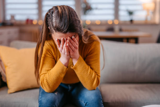 悲しくて取り乱しているように見える家で一人で座っている若い女性 - 困った ストックフォトと画像