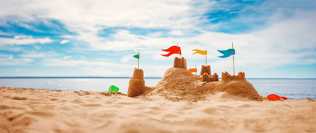 Sand castle with colourful flags on the beach of the sea. Panoramic view. Concept of the vacation and tourism.