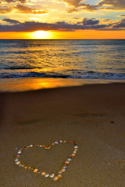 People walking on a sandy beach at sunrise. Heart shape hand drawing on the beach.