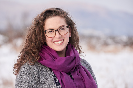 Portrait of a young woman wearing a jacket and sweater smiling while out for a winter walk in nature