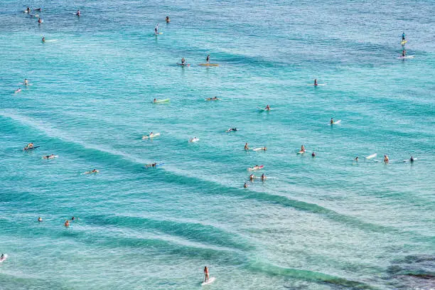 Aerial view of beach travel vacation Hawaii holiday with surfers people swimming in blue ocean water surfing on waves with surfboards, sup paddle boards. Watersport activity summer sport lifestyle. Waikiki Beach, Honolulu, Oahu, Hawaii
