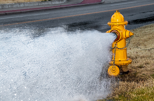 Yellow fire hydrant by four-lane street  gushing water on a winter day