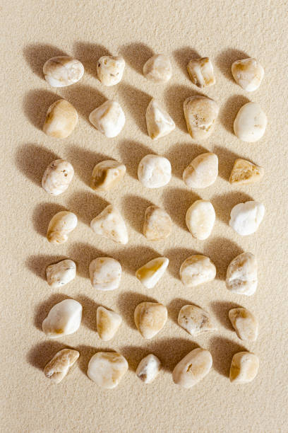 istock Pattern with white pebble sea stones on fine sand. Square composition from natural stone neutral beige color, monochrome tones. Spa minimal background 1371341632