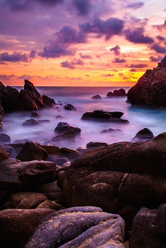 Sunset on the sea with a sky of colors reflected in the clouds Long exposure photography that captures the movement of the waves between the rocks of the coral beach in Puerto Escondido Oaxaca