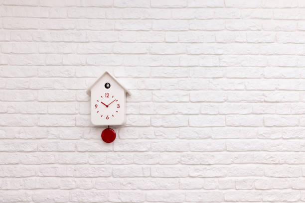istock Cuckoo bird clock with red pendulum on a white brick wall 1371342314