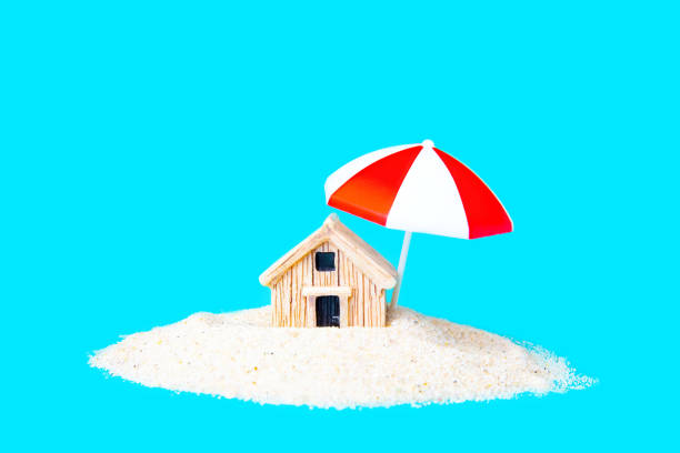 Toy house in sand under a parasol on blue