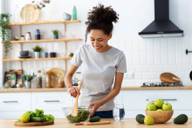 Healthy diet eating. African American young female preparing salad in home kitchen. Beautiful woman cooking healthy food, breakfast or dinner stock photo