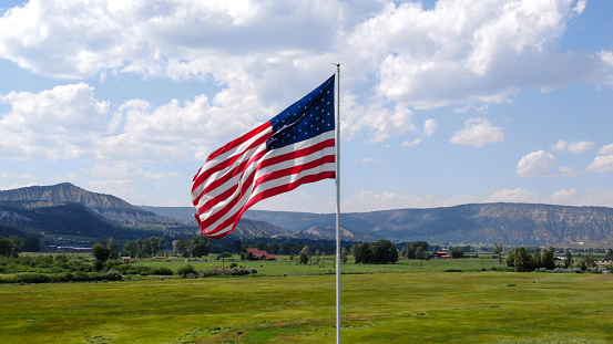 American Flag Flying in a meadow nestled in the rocky mountains in southwestern Colorado near Telluride and Ouray on a bright partly cloudy day with beautiful clouds