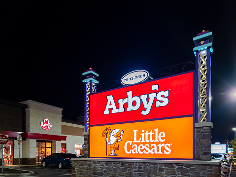 Orlando, Florida - February 4, 2022: Closeup Night View of Arby's and Little Caesars Billboard in Foreground and Arby's Building in Background