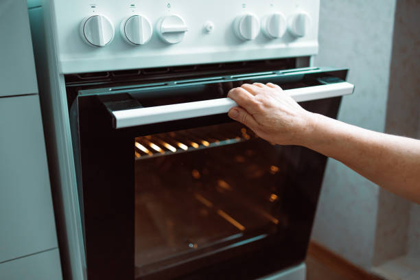 woman hand opening oven door and light is on in kitchen at home. - oven imagens e fotografias de stock