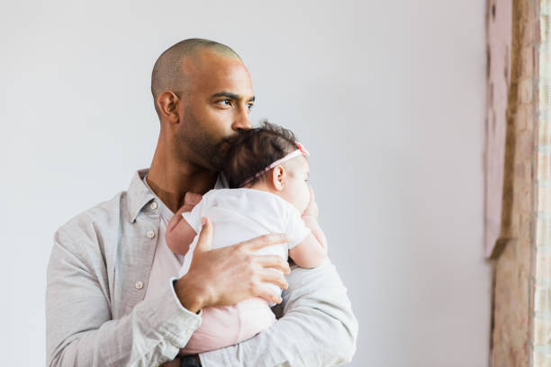 Stay-at-home dad looks out window while carrying baby