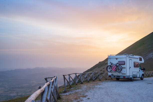 istock Camper van on road side in beautiful landscape. Dramatic sky at sunset, scenic clouds above unique highlands and hill range in Italy, alternative vanlife vacation concept. 1371356468