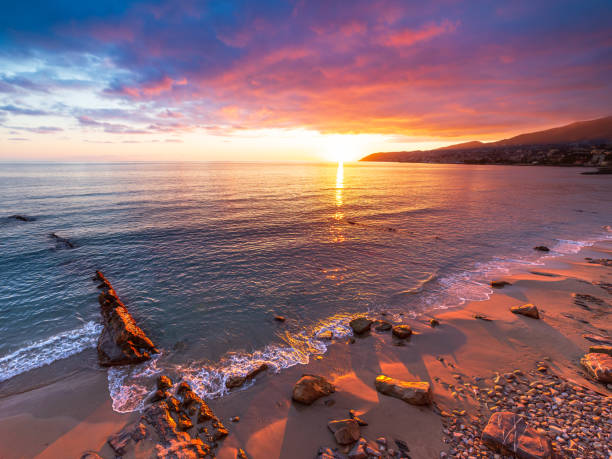 sanremo, riviera dei fiori, liguria, włochy. scenis skały i kamyki na plaży oświetlone pięknie przez światło zachodu słońca. dramatyczne kolorowe niebo falujące morzem. - san remo zdjęcia i obrazy z banku zdjęć