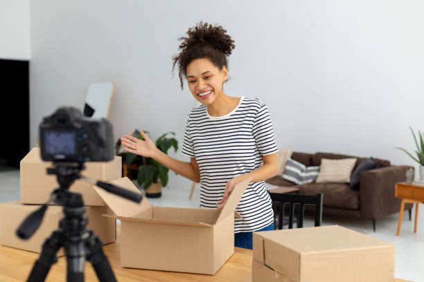 istock African American female blogger vlogger freelancer using camera to recording video content for his followers, makes an overview of the products, goods. Young woman unpacking boxes on camera 1371356763