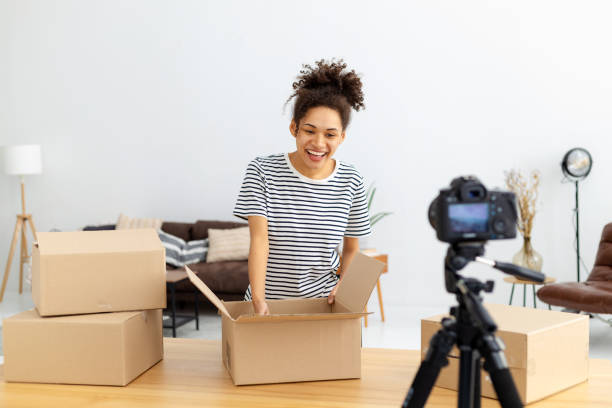 istock African American female blogger vlogger freelancer using camera to recording video content for his followers, makes an overview of the products, goods. Young woman unpacking boxes on camera 1371356787