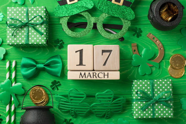 Top view photo of st patricks day decor wooden cubes calendar 17 march party glasses straws green bow-tie gift boxes horseshoe shamrocks pots with gold coins on isolated green wooden table background foto de la vista superior del día de san patricio decoración cubos de madera calendario 17 copas de fiesta de marzo pajitas verde pajarita cajas de regalo tréboles de herradura ollas con monedas de oro sobre fondo de mesa de madera verde aislado