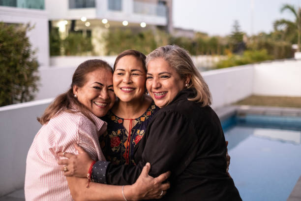 Female Latin friends hugging each other and laughing at home stock photo