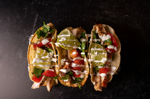Gourmet Chicken Street Tacos lined on a metal serving rack with tomato salsa, sour cream and cilantro ready to eaten. Authentic Mexican Cuisine on a dark back ground with studio lighting to make the taco stand out.