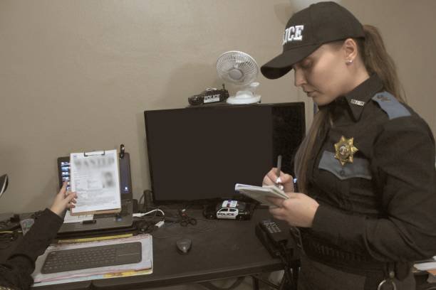 Female police officers, blue uniform two female police officers in office taking notes, looking at computer, consulting with each other, full uniform female police officer stock pictures, royalty-free photos & images