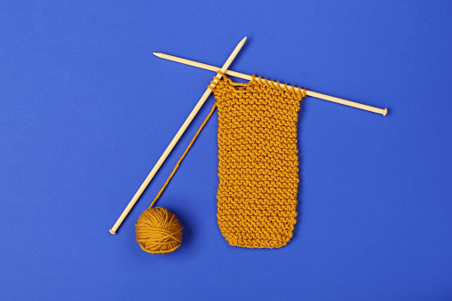 Knitting with needles on colored paper backdrop.