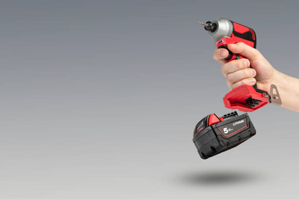 istock Drill in hand on a gray background. Cordless drill or screwdriver without a battery in a man's hand, a removable lithium battery floating in the air. The concept of selling and using cordless tools 1371370785