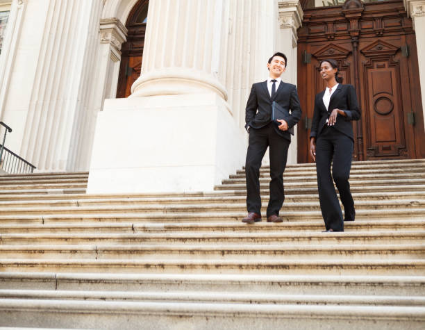 Legal Business People A well dressed man and woman smiling as they as they walk down steps of a courthouse  building. Could be business or legal professionals. politics stock pictures, royalty-free photos & images