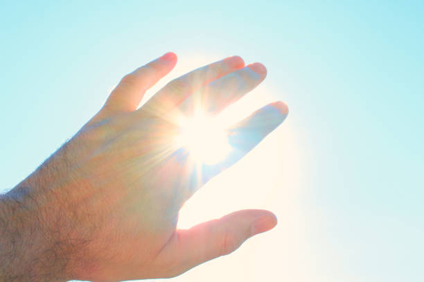 Male hand covers the sun. The sun's rays shine through the hand. Close-up. Background. Texture. stock photo