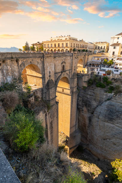 vertikale porträtansicht der schlucht, der altstadt und der brücke puente nuevo in der mittelalterlichen stadt ronda, spanien, in der region südandalusien mit einem farbenfrohen sonnenuntergang, der das dorf hervorhebt. - malaga seville cadiz andalusia stock-fotos und bilder