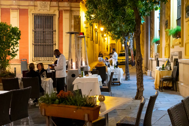 Servers take orders with face masks on at an outdoor sidewalk cafe in the Barrio Santa Cruz district of Seville, Spain. Servers take orders with face masks on at an outdoor sidewalk cafe in the Barrio Santa Cruz district of Seville, Spain. santa cruz seville stock pictures, royalty-free photos & images