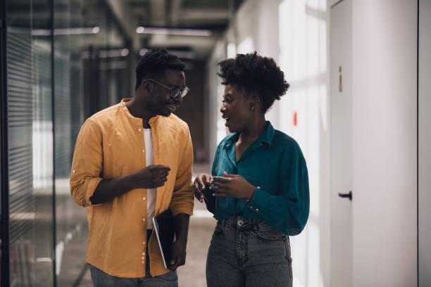 istock Two young attractive black  coworkers talking and smiling in office hallway 1371405496