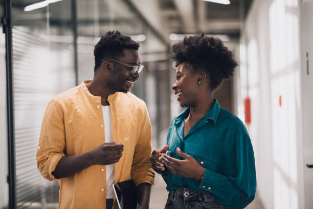 Two black confident businesspersons talking and smiling in work space