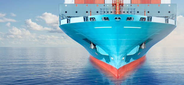 Front view of large blue container cargo ship in ocean waters. Performing cargo export and import operation. Front view of large blue container cargo ship in the ocean. Performing cargo export and import operations with horizon line and beautiful sky. boat front view stock pictures, royalty-free photos & images
