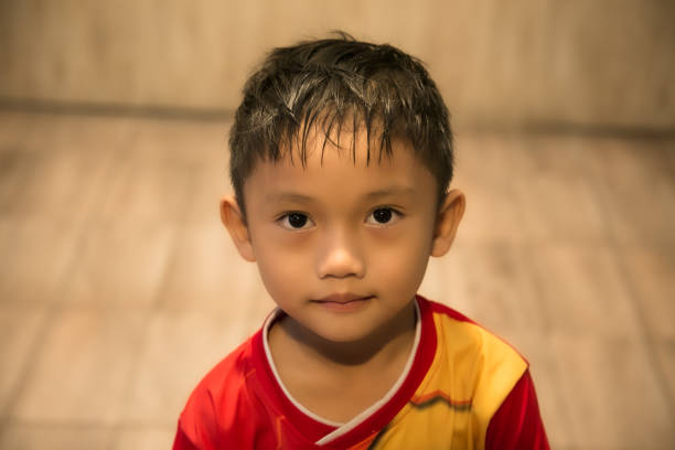 Toddler boy is playing with curtains at home. Small kid making fun face expressions.